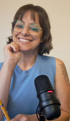 Foto de Vânia Santiago do tórax para cima. 

Ela está de frente a um fundo bege. 

Usa uma blusa azul bebê sem mangas e óculos de grau com armação transparente. 

Sorri de forma alegre. 

Seus cabelos castanho-escuros estão na altura da nuca e levemente ondulados.

A mão direita dela está tocando o queixo. Suas unhas estão pintadas de nude. 

Ela segura uma caneta amarela na mão esquerda. O braço esquerdo está repousado sobre uma mesa, ao lado de um microfone de podcast. Ainda no braço esquerdo, nota-se parte de uma tatuagem de folhas com traço delicado.